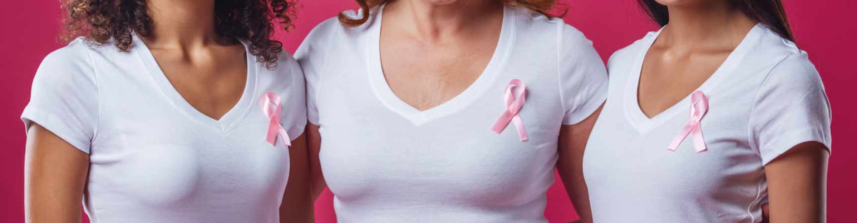 tre donne in maglietta bianca con il nastrino rosa incrociato appuntato all'altezza del seno sinistro